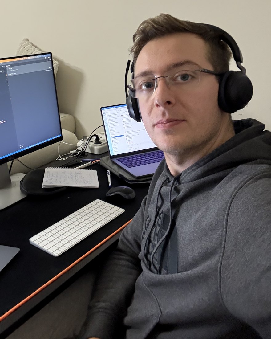Boris Dedejski at his desk in Amsterdam, wearing headphones, with code on the monitor behind him